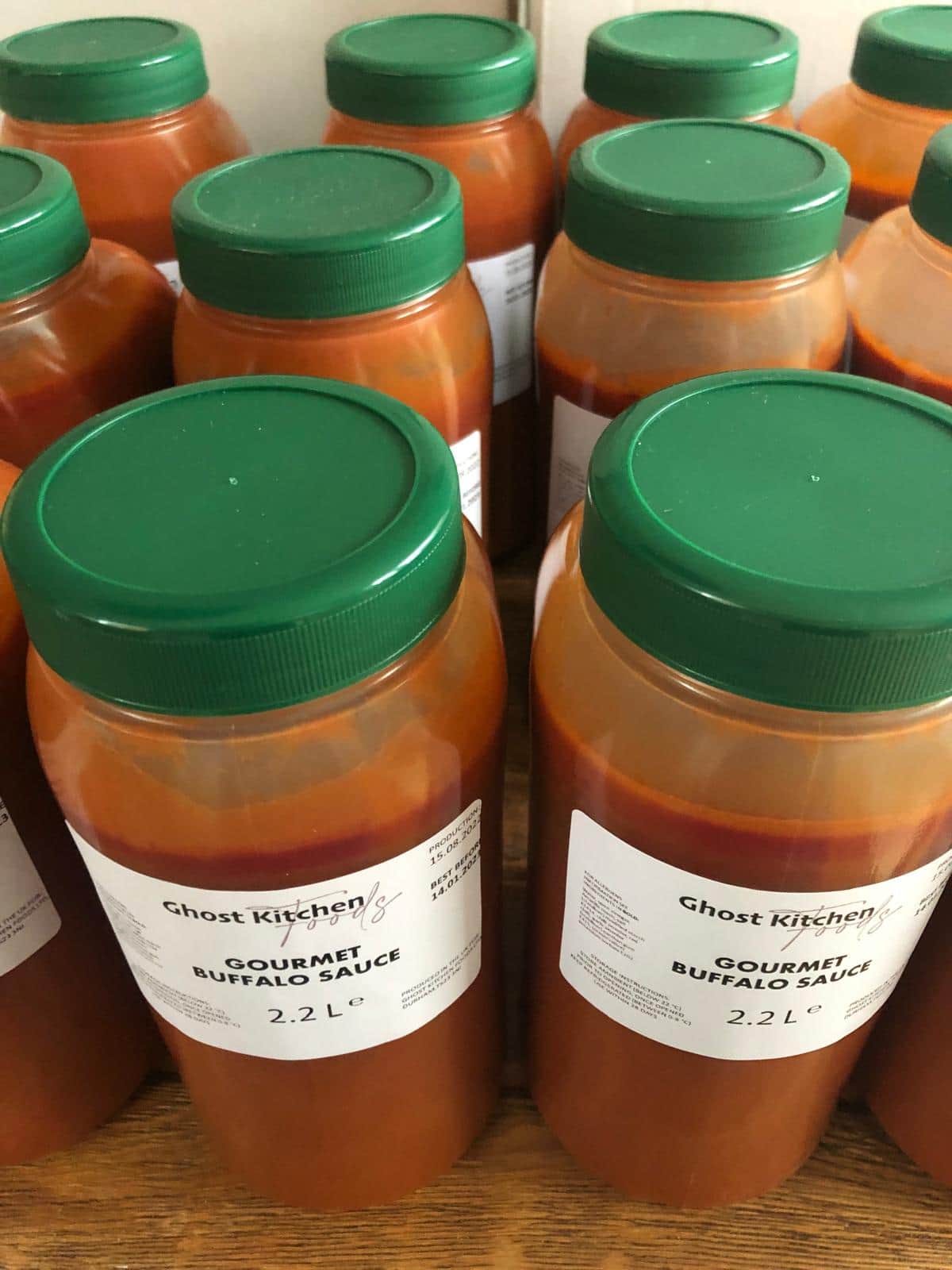 Rows of Ghost Kitchen Foods Gourmet Buffalo Sauce in 2.2 litre tubs with green lids