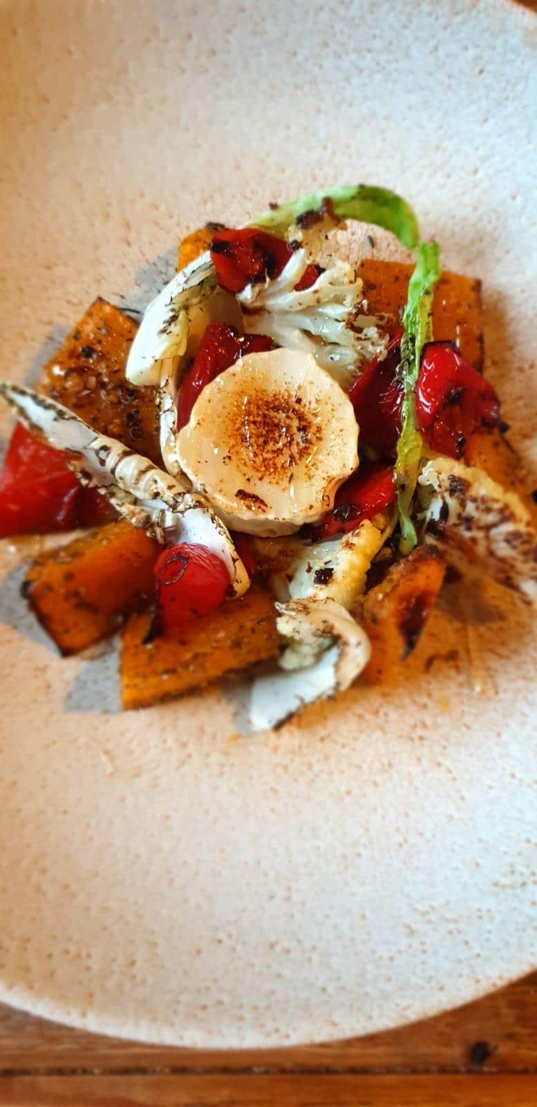 Roasted squash, red peppers and charred cauliflower with a disc of grilled goat's cheese on a speckled plate
